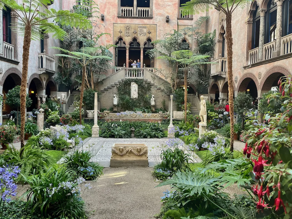 the interior courtyard at eh isabella sterwart gardener museum in boston is a lish garden within venetian walls with romand venetian statues and stonework.