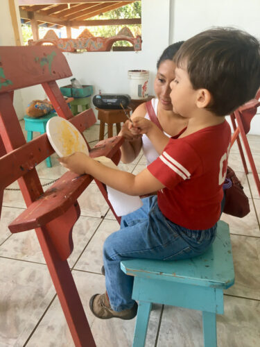 a young boy tries to mimic the colorful paint on a sarchi ox-cart wheel.