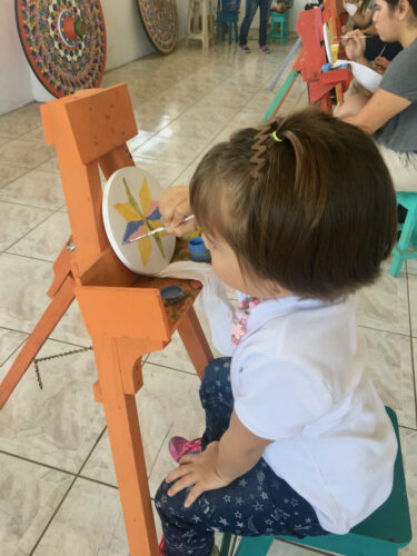 A young girl paints a small imitation of a sarchi cart wheel.