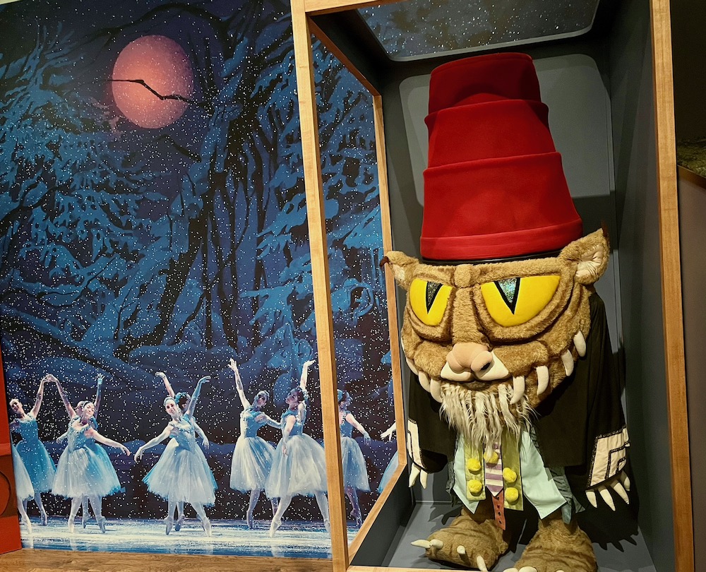 A costume for a turkish-hat-wearing creature from maurice sendak's nutcracker suite with a mural of dancers on a snowy night alongside it.