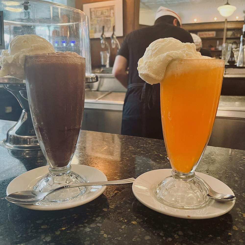 A black & white float and a creamsicle float on the counter of brooklyn farmacy with a soda "jerk" in the background.