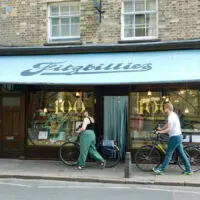 Fitzbillies café is an essential stop on any visit to Cambridge with teens. Two people with bikes pass under its blue awning.