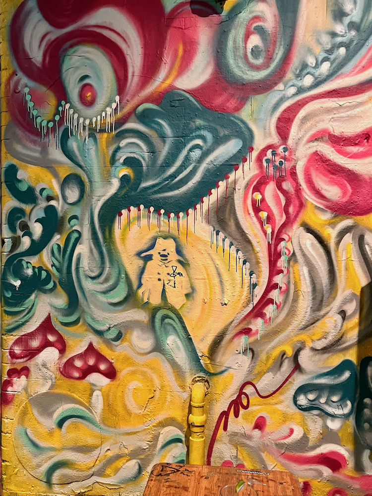 In the graffitti tunnel below waterloo station, paddington bear is surrounded by green, red and yellow psychadelic swirls.