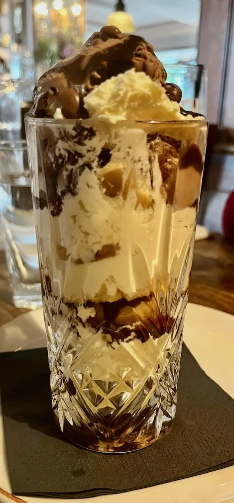 this knickerbocker glory at the mad hatter pub stacks profiteroles, ice cream, chocolate syrup and whipped cream.