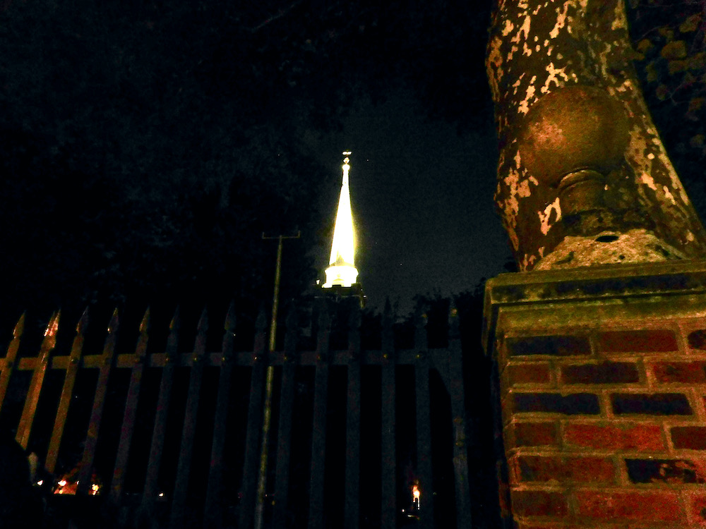 A church steeple lit up at night as seen through a cemetary gate in philadelphia.