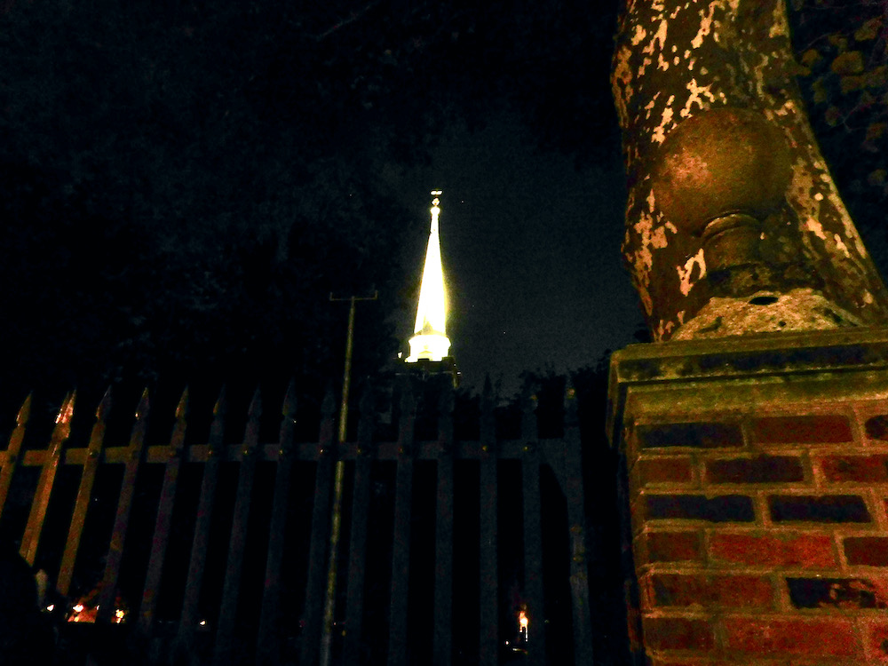 a church steeple lit up at night as seen through a cemetary gate in philadelphia.