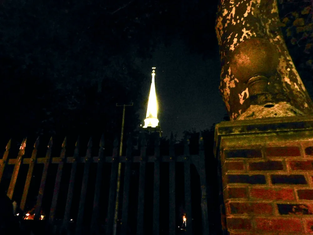 a church steeple lit up at night as seen through a cemetary gate in philadelphia.