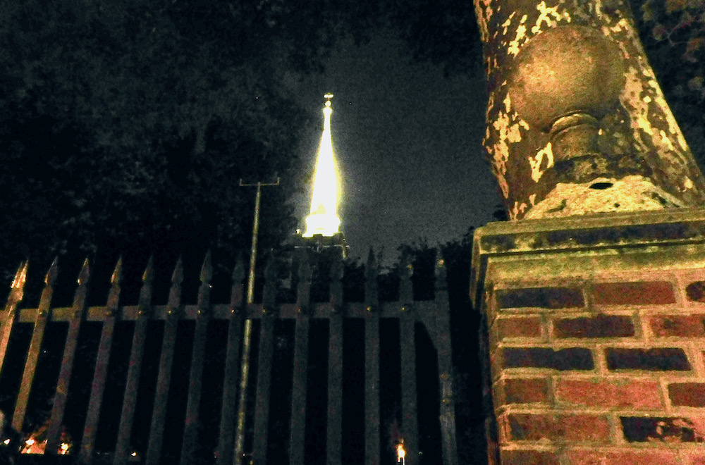 A philadephia cemetary gate with a tower lit up behind it looks ghostly at night.