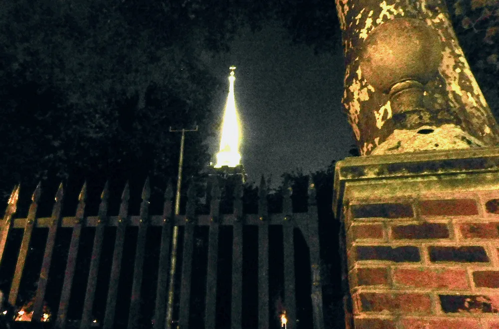 a philadephia cemetary gate with a tower lit up behind it looks ghostly at night.
