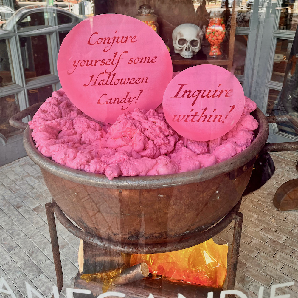 A halloween window at shane's candy store features  skulls andn a cauldron of something sweet.