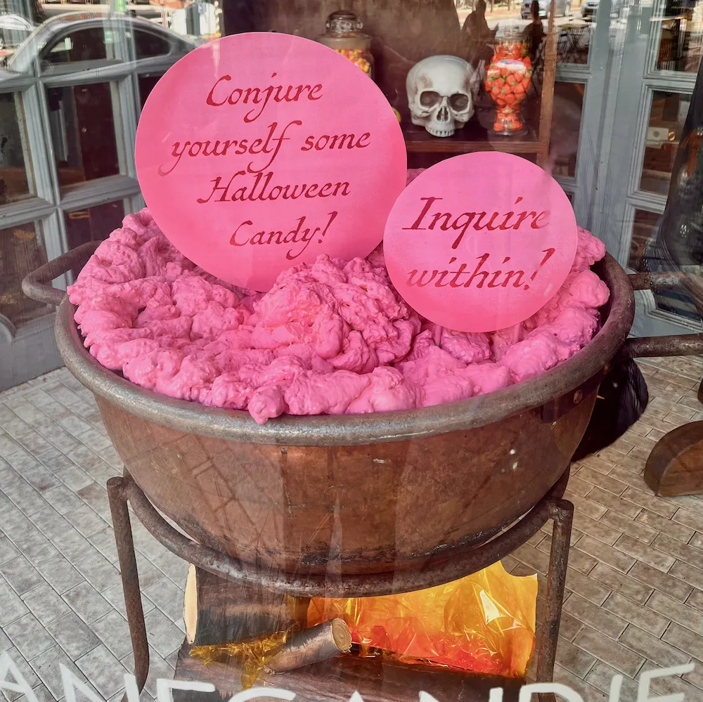 a halloween window at shane's candy store features  skulls andn a cauldron of something sweet.