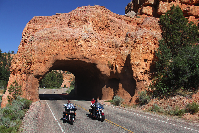 2 motorcyclists pass under a red-rock tunnel on scenic byway 12 in utah.