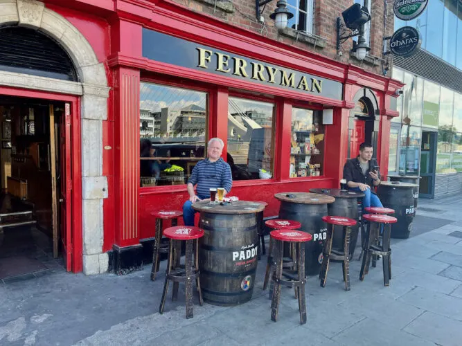 men enjoy a pint on stools next to barrels out the ferryman, a frendl docklands pub.