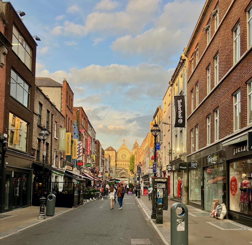 a busy pedestriam shopping street in low-rise dublin, with a church at the end of it.