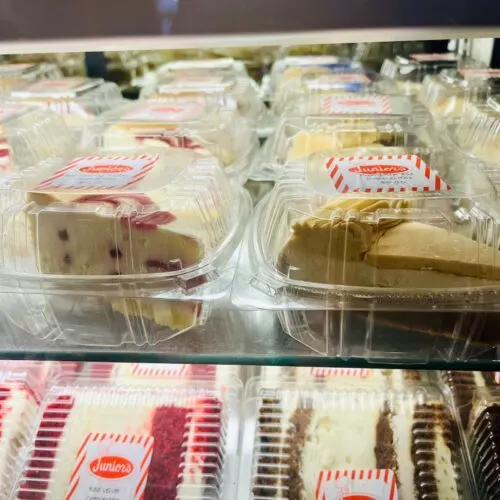 a window display of slices of junior's pumpkin and strawberry swirl cheesecakes and chocolate and red velvet cakes.