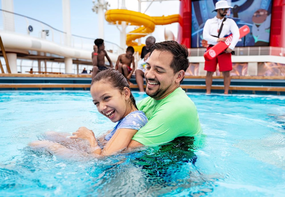 Dad and daughter play in s disney cruise line pool while a lifeguard looks on.