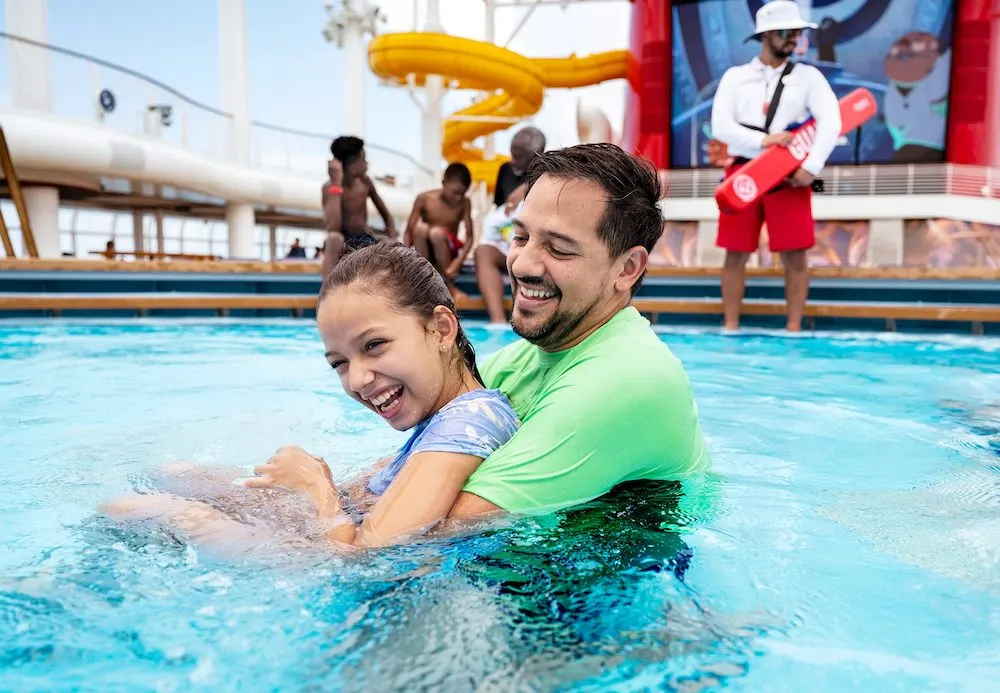 dad and daughter play in s disney cruise line pool while a lifeguard looks on.