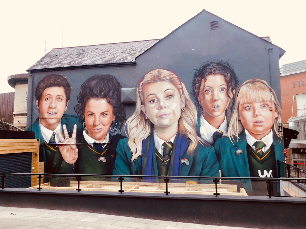 a derry girls mural celebrates the hit show on a wall it namesake city. teens love the local walking tour.