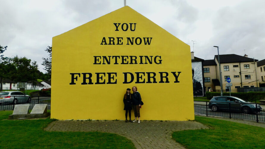 a teen and her mom pose in front of the iconic entering free derry mural during a walking tour of the city.