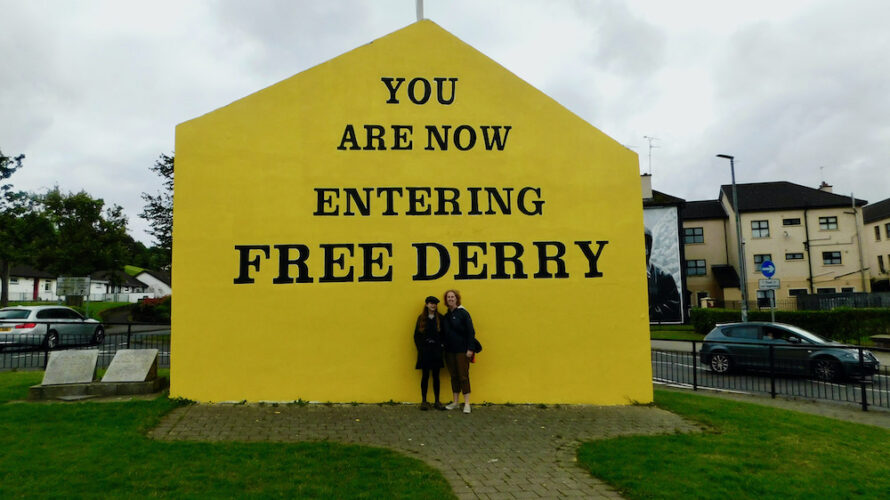 A teen and her mom pose in front of the iconic entering free derry mural during a walking tour of the city.