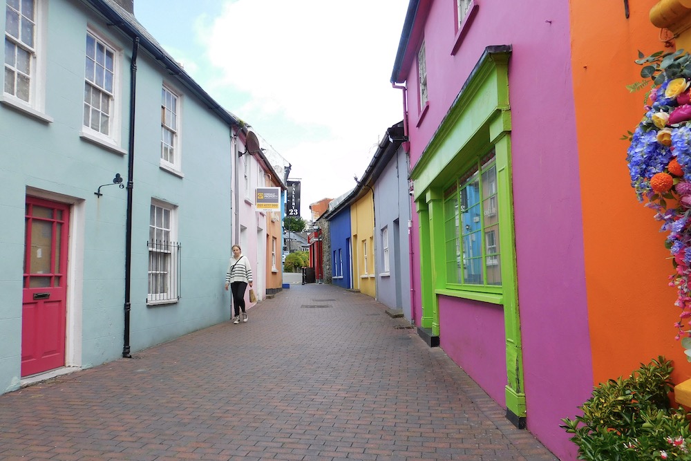 Pink, yellow, turquoise and blue attached houses line up on either side of a narrow brick street in kinsale, ireland