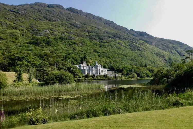 castle-like kylemore abbey sits nestled between green foothalls and a glassy lake.