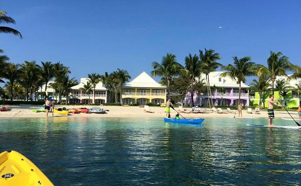 guests paddleboard and kayak near the beach with old bahama bay's colorful buildings behind them.