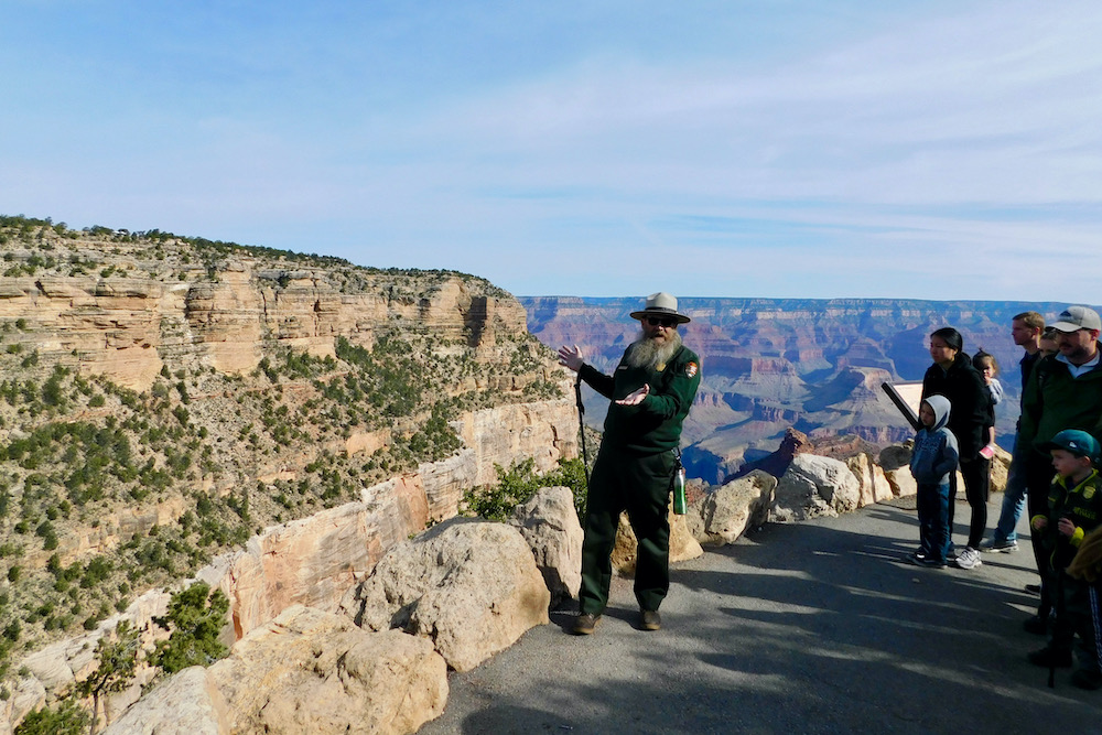 Grand canyon national park's rim trail is flat, paved, has incredible views and is accessible to mobility impared visitors. Here range talks about rocks along the trail.