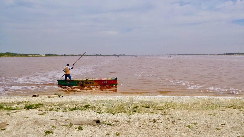 a man in a senegalese flat boat harvests salt from lac rose.