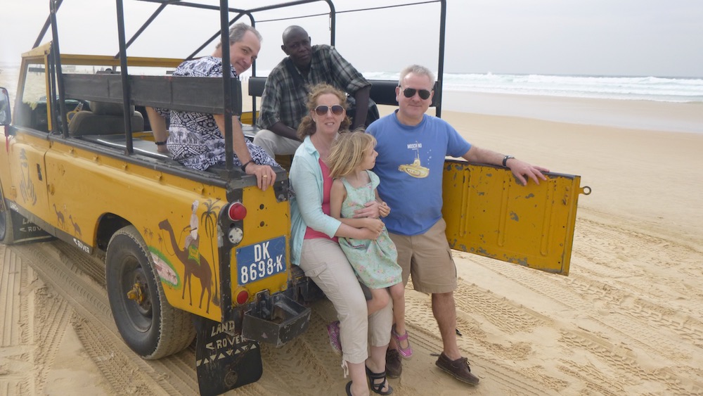 a family poses in the back of a beat-up 4wd jeep on a beach in senegal.