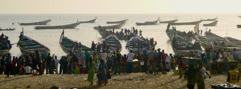 Crowds meet the returning fishing piroges at the beachside fish market in mbour, senegal.