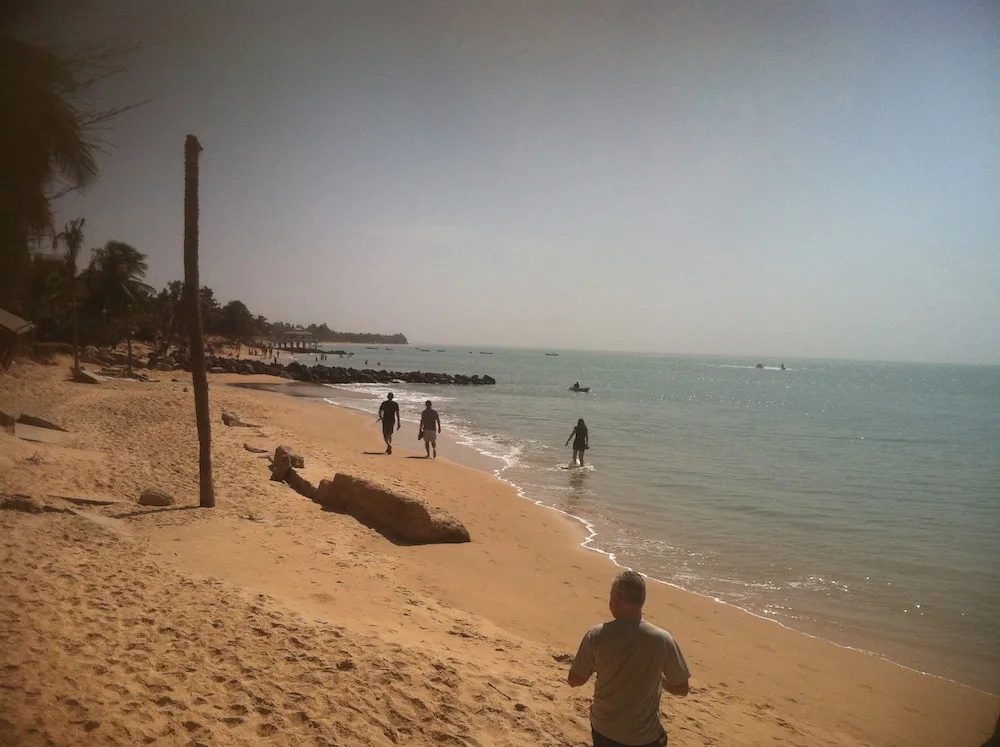 people walk on a long stretch of yellow sand on saly beach in senegal.