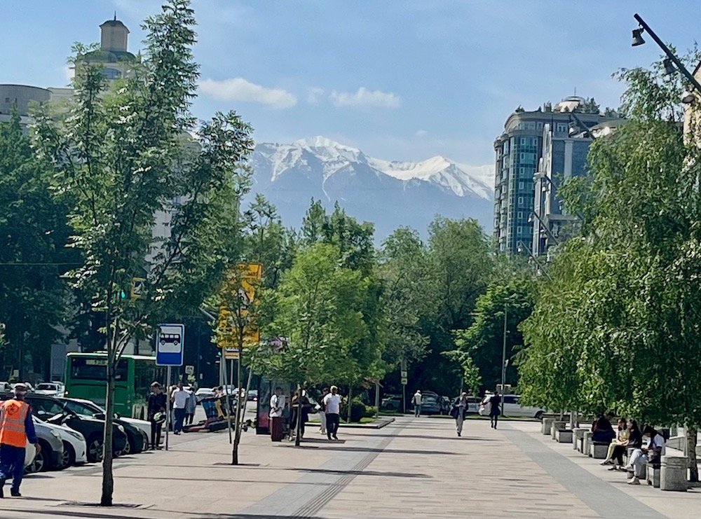 almaty, kazakhstan is a modern city with wide, tree-line streets and mountains in the distance.