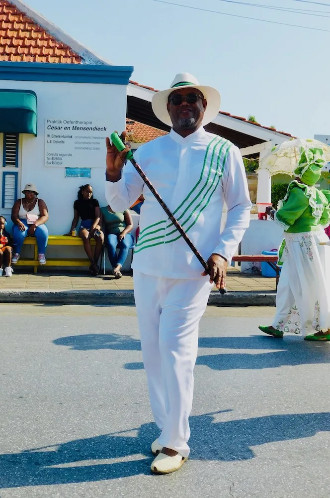 a man dressed in green and white pauses on the harvest parade route into willemstad