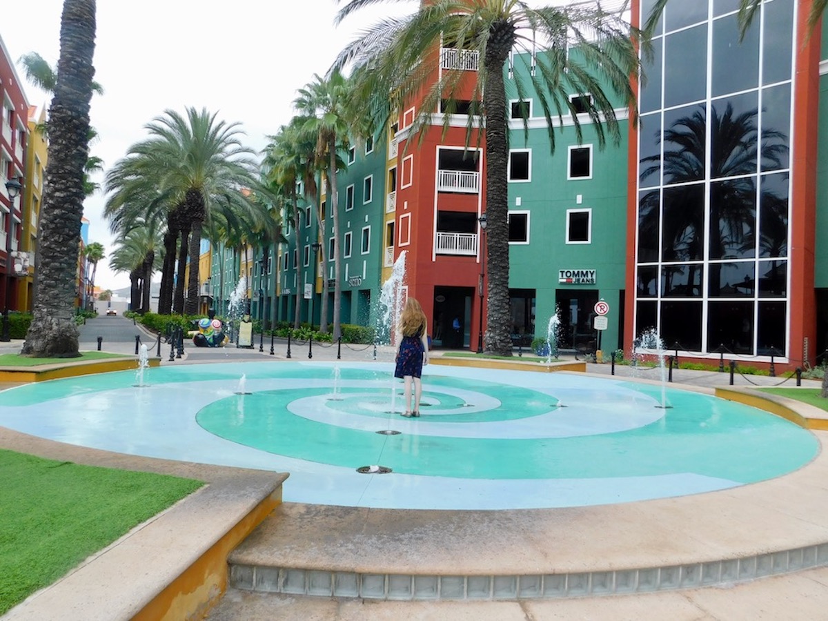 6 Top Things To Do To Explore Colorful Curacao WIth Kids: A girl walks through a play fountain outside the Rif Fort in Curacao