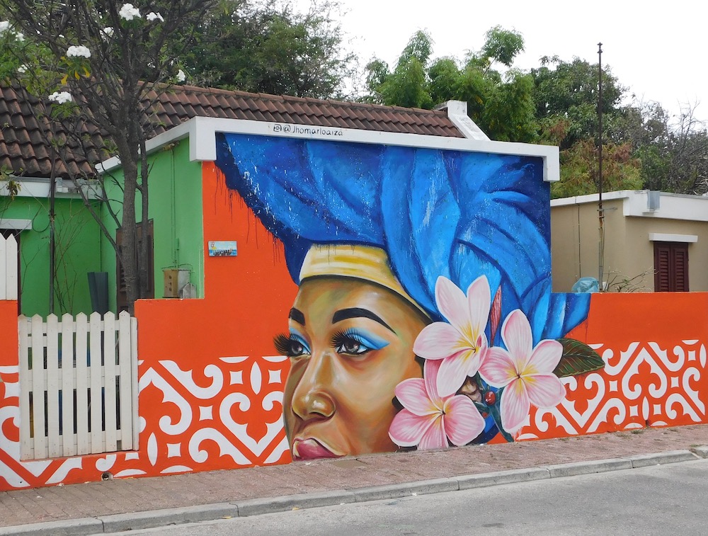 a mural of a curacao women in a blue headdress on the of a house on arubastraat. 
