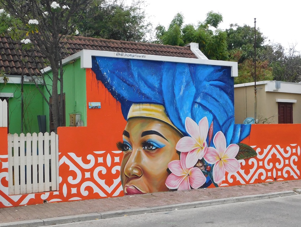 A mural of a curacao women in a blue headdress on the of a house on arubastraat.