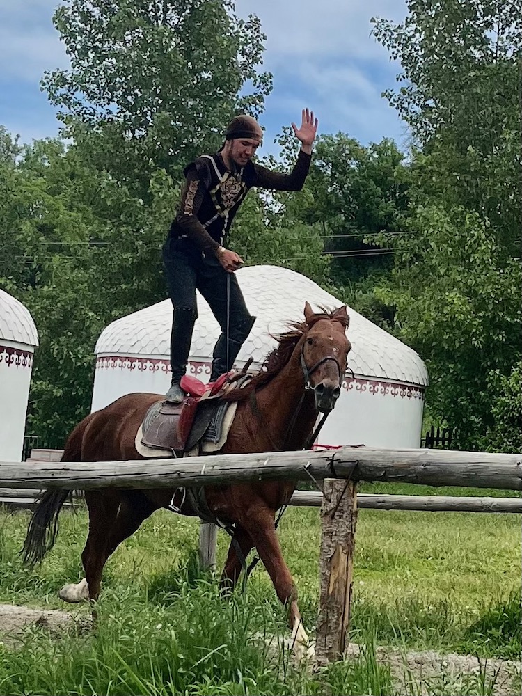 A male stunt rider stands on a moving horse at the huns ethno-village, a fun thing to see with kids in kazakhstan