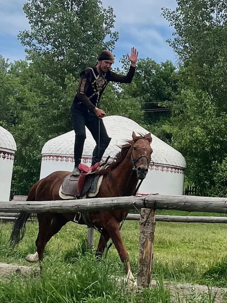 a male stunt rider stands on a moving horse at the huns ethno-village, a fun thing to see with kids in kazakhstan