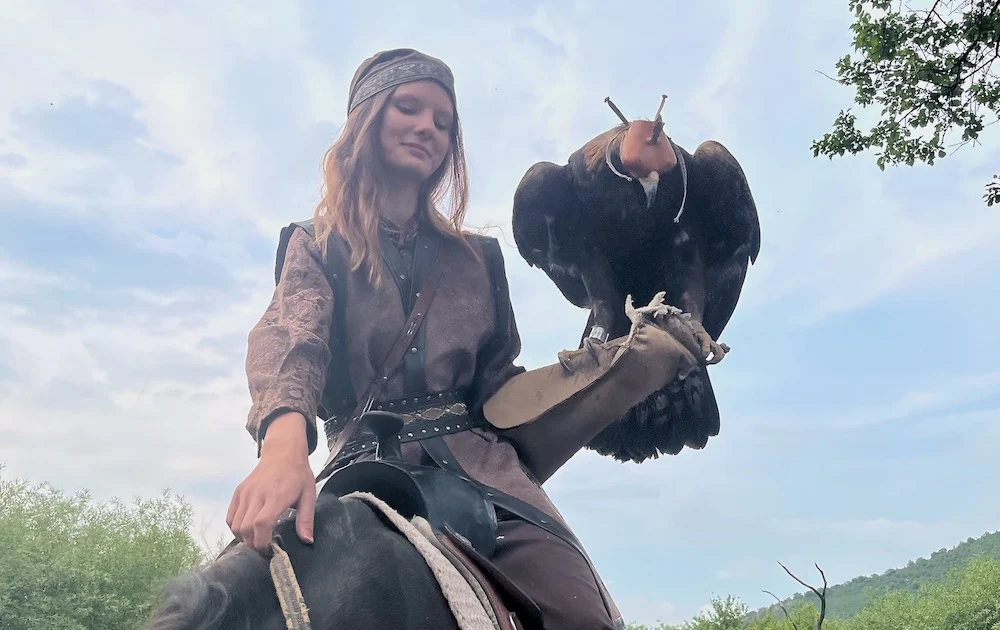 a women rides a horse with a falcon on her arm at the sunkar raport sanctuary's bird of prey show.