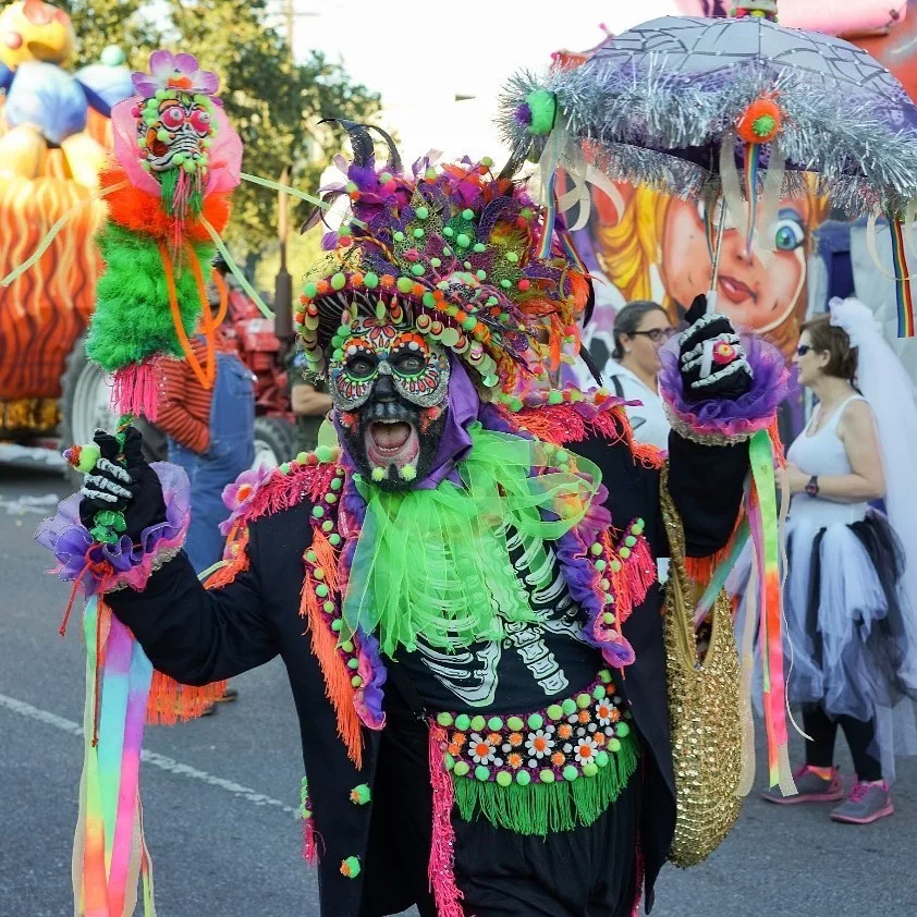 a man in a day of the dead mask in mardi gras colors at the krewe of boo parade in new orleans
