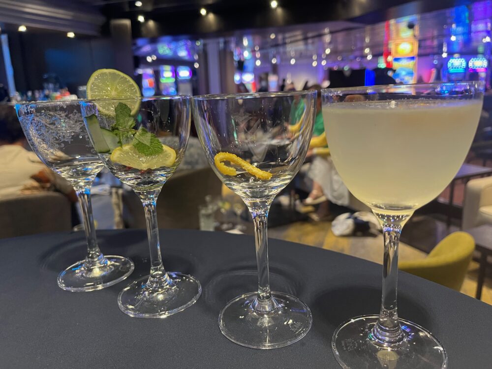 4 cocktail glasses lined up with a gin cocktail in one and anticipatory garnishes in the other three.