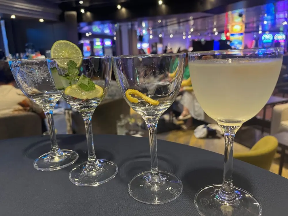 4 cocktail glasses lined up with a gin cocktail in one and anticipatory garnishes in the other three.