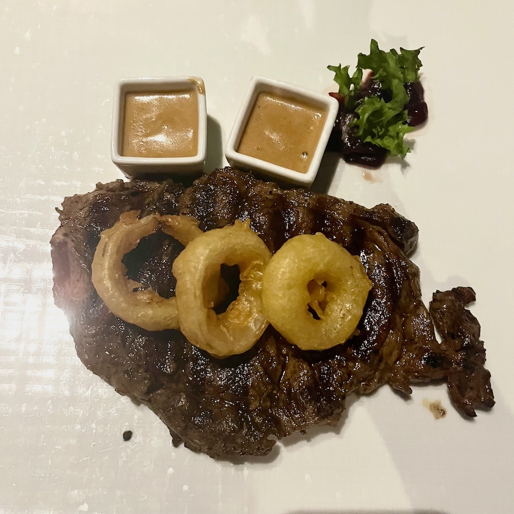 holland america's pinnacle grill serves steak with fat onion rings and sauce on the side.