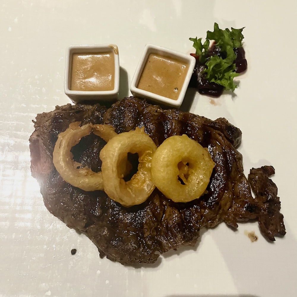 Holland america's pinnacle grill serves steak with fat onion rings and sauce on the side.