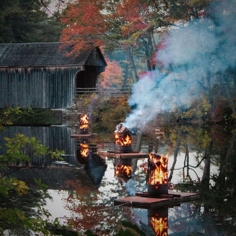 at sturbridge village for halloween, lanterns float on water leading visitors to a covered bridge for halloween-season evening activities.