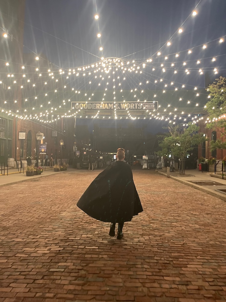 a caped tour guide leads people on a haunted walk around the distillery district in toronto