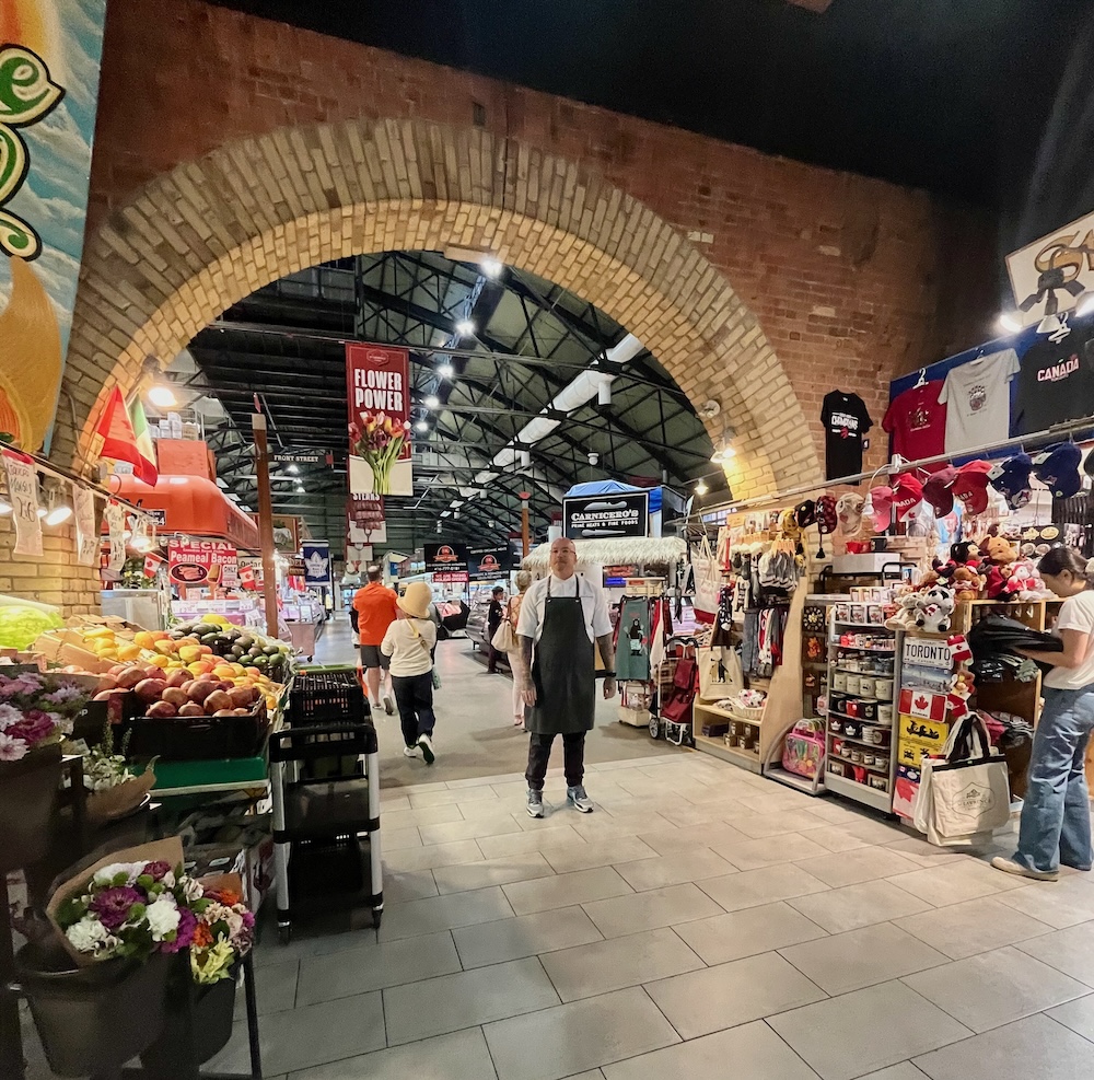 a chef stands at the arched entrance to the st. lawrence market in toronto's old town.