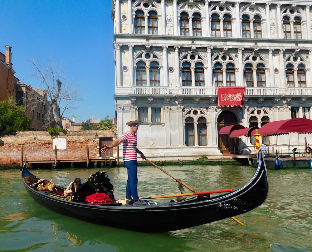 a gondolier steers passed a white palazzo with venetian style arched windows.