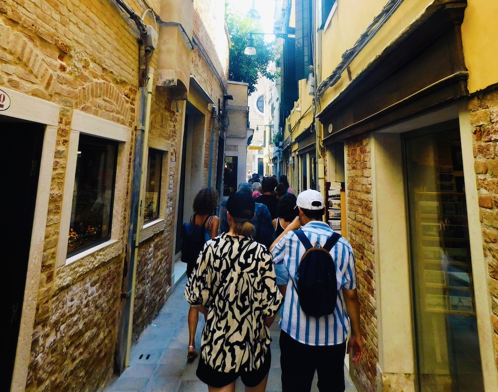 a steady stream of tourists makes their way down a narrow alleyway in venice; these crowds can make the city challenging to explore with kids.